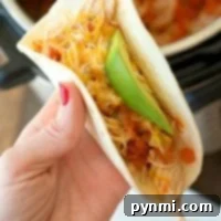 A hand holding a taco filled with shredded cheese, avocado, and tomato, alongside tender instant pot salsa chicken.