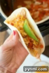 Zesty Instant Pot Salsa Chicken 6 A hand holding a taco filled with shredded cheese, avocado, and tomato, alongside tender instant pot salsa chicken.
