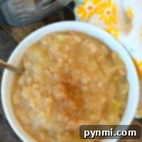 A bowl of apple cinnamon applesauce sits invitingly beside a pressure cooker, with a floral cloth adding a touch of charm.