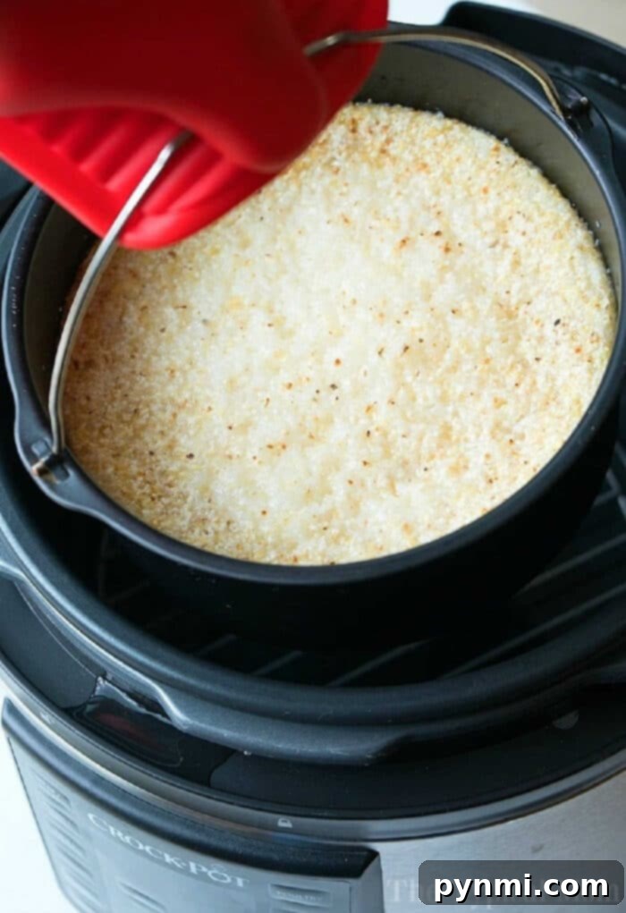 A red oven mitt lifts a pan of golden-browned, baked dish from a black pressure cooker, as if serving up warm Instant Pot grits.
