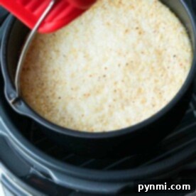 A red oven mitt lifts a pan of golden-browned, baked dish from a black pressure cooker, as if serving up warm Instant Pot grits.