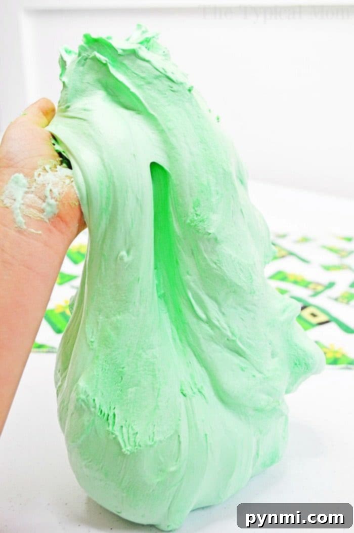 Make fluffy green slime with shaving cream and 2 other ingredients, completely borax-free and kid-safe for St. Patrick's Day or any fun occasion. A child's hands stretching vibrant green fluffy shaving cream slime, showcasing its soft and pliable texture.