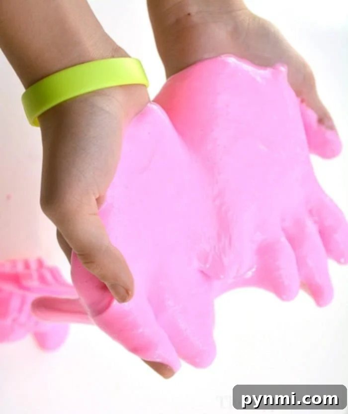 A close-up view of homemade pink glow-in-the-dark slime, highlighting its stretchy texture and brilliant color. A super easy and fun craft project for kids, perfect for birthdays or school holidays. Close-up of pink glow in the dark slime being stretched, showing its elasticity and vibrant color even in daylight.
