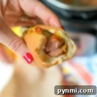 A hand holds a bitten hot dog with mustard and ketchup, the vibrant red nails adding a pop of color. Perfectly cooked using an Instant Pot, this hot dog promises both convenience and flavor in every bite.