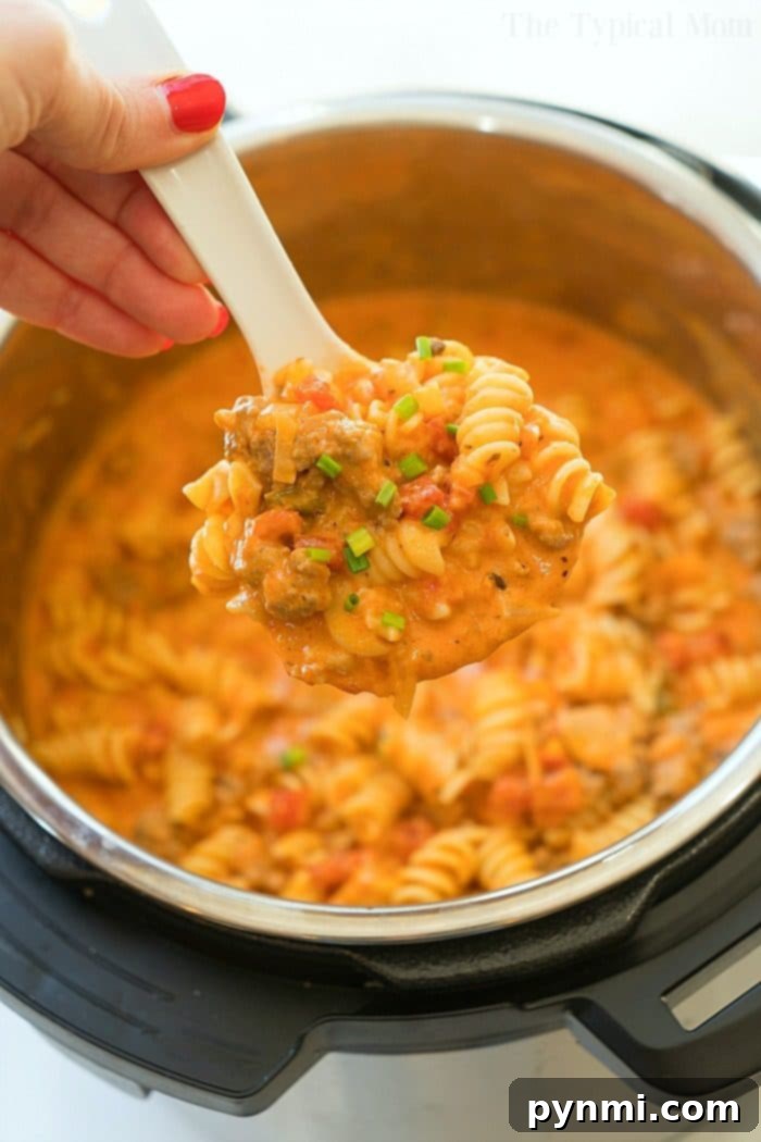 Cheesy Instant Pot goulash turned out amazing in my pressure cooker! Creamy goulash with the same flavors you love with two different cheeses within it too. Total comfort food in your pressure cooker that will be your kid's new favorite dinner for sure. #instantpot #pressurecooker #goulash #cheese #cheesy #pasta #casserole #instantpotrecipes #thetypicalmom Close-up of hearty Instant Pot goulash featuring rotini pasta, ground meat, and a rich, creamy tomato sauce, garnished with fresh parsley.
