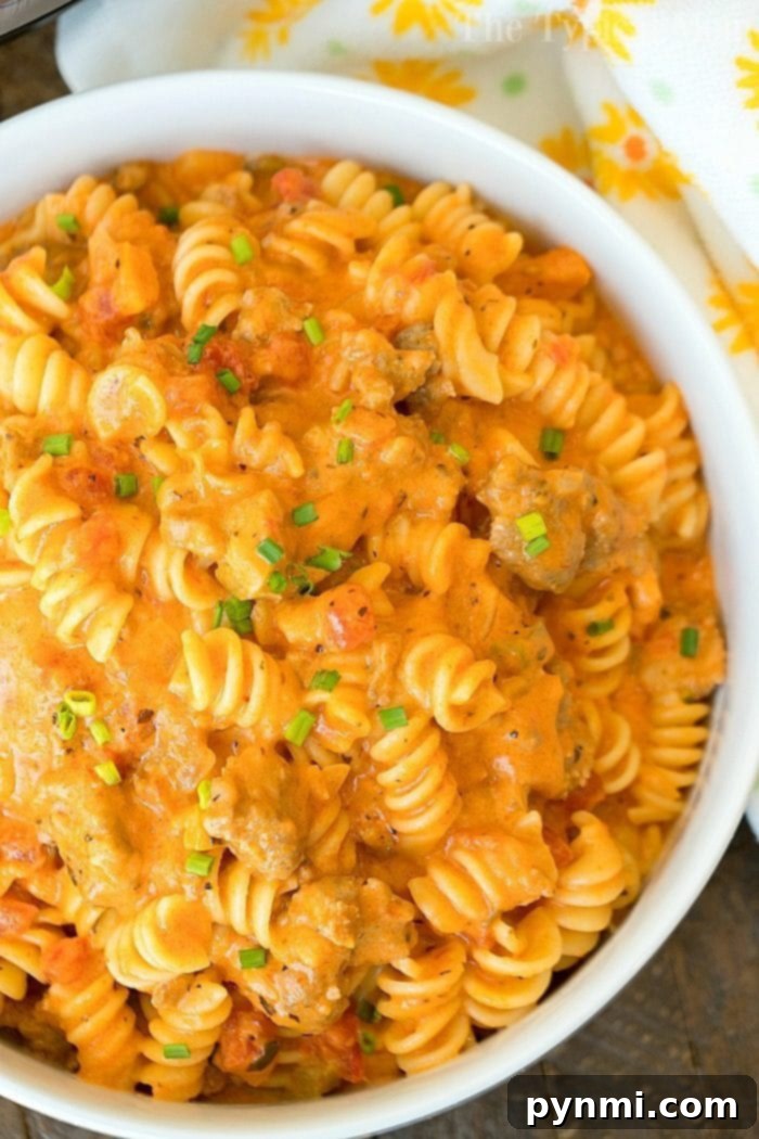 Cheesy Instant Pot goulash turned out amazing in my pressure cooker! Creamy goulash with the same flavors you love with two different cheeses within it too. Total comfort food in your pressure cooker that will be your kid's new favorite dinner for sure. #instantpot #pressurecooker #goulash #cheese #cheesy #pasta #casserole #instantpotrecipes #thetypicalmom A top-down view of a bowl of cheesy Instant Pot goulash, garnished with fresh chives, with a spoon ready to serve. The pressure cooker sits in the background.