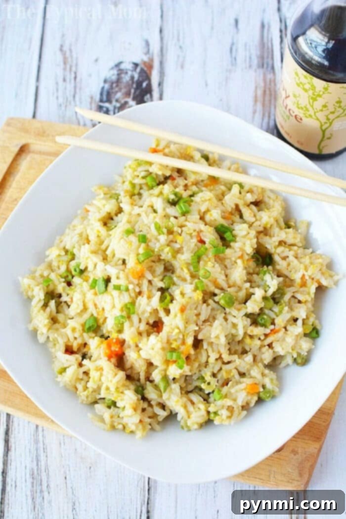 Savory pressure cooker fried rice, complete with egg and vegetables, ready to enjoy. A plate of pressure cooker fried rice with chopsticks sits on a wooden board next to a bottle of soy sauce.