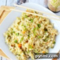 Perfect Pressure Cooker Fried Rice 2 A plate of pressure cooker fried rice with peas and carrots rests on a wooden board, accompanied by chopsticks and a bottle of soy sauce.