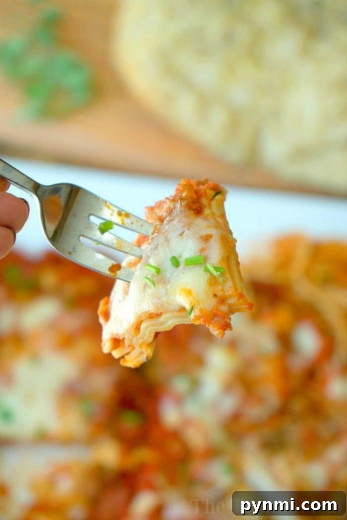 A fork holding a cheesy lasagna piece, garnished with herbs, with more lasagna and slow cooker rolls in the background.