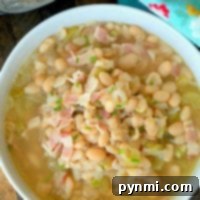 A bowl of pressure cooker bean soup with bacon bits, garnished with herbs, sits next to a patterned cloth.