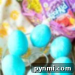 Blue dyed eggs rest elegantly on a metal stand, while a basket brimming with Kool-Aid packets and decorative yellow grass sits in the background. Discover how to dye eggs with Kool-Aid for vibrant hues that brighten any table setting.