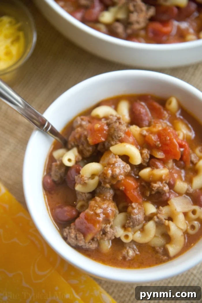 A steaming bowl of Instant Pot Chili Mac, topped with melted cheese and fresh green onions, served next to the Instant Pot