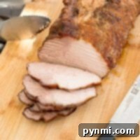 Sliced roasted pork loin rests on a wooden cutting board after being smoked, showcasing its tender interior. A knife and tongs sit nearby, ready for serving.