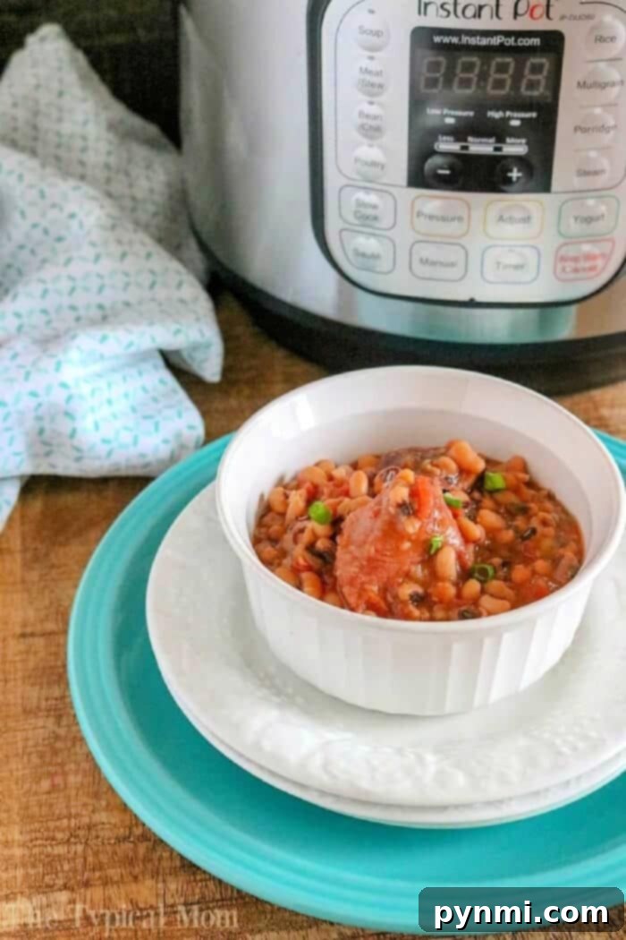 A white bowl of hearty bean stew, featuring pressure cooker black eyed peas and ham, sits ready to serve next to an Instant Pot on a rustic wooden surface.