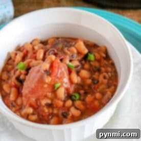 A white bowl filled with pressure cooker black eyed peas and ham in broth, garnished with green onions, ready to be served.