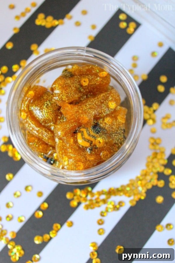 Make your own honey slime with clear glue, gold glitter, and fun plastic bees. This easy DIY craft is perfect for kids and parties. #honey #slime #gold #glitter #glue #easy #ingredients A jar of golden, glittery gummy bears that look like honey slime, with sequins on a black and white striped background.