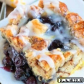 A glazed blueberry pastry on a white plate, with layers of bread and visible cherry filling, evokes the comforting warmth of a cinnamon roll—a delightful breakfast casserole treat.