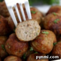 A fork holds a halved meatball above a pile of perfectly cooked, flavorful spheres, garnished with fresh herbs. These delectable bites are straight from frozen meatballs in an air fryer for that crispy perfection.