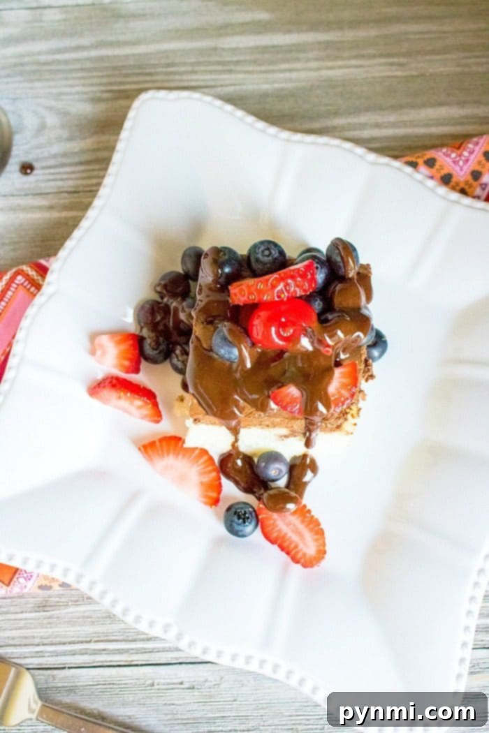 poke cake topped with chocolate sauce, strawberries, and blueberries on a white plate with a patterned napkin nearby, this delightful treat might inspire you to explore how to make a poke cake next time.