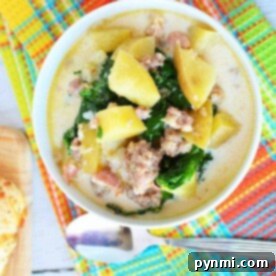 A bowl of creamy pressure cooker zuppa Toscana with potatoes, sausage, and kale rests on a colorful tablecloth beside a spoon.