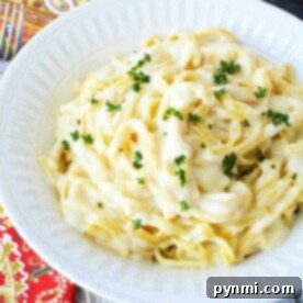 A white bowl filled with creamy Instant Pot fettuccine alfredo, garnished with chopped parsley. The bowl is placed on a colorful patterned tablecloth, with a fork nearby.