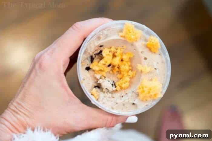 A close-up of a clear plastic cup containing a creamy, light dessert topped with crumbled 2-ingredient orange soda cake, suggesting a low-calorie or dairy-free treat.