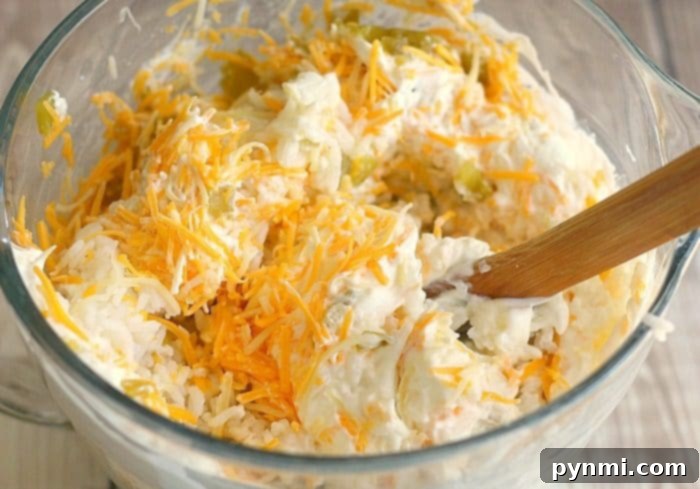 Great green chile rice side dish you can make and serve during the holidays or throughout the year for dinner. Cheesy and full of flavor! #green #chile #chiles #hatch #casserole #rice A clear glass baking dish brimming with a creamy, cheesy green chile rice mixture, ready for the oven, with a wooden spoon resting nearby.