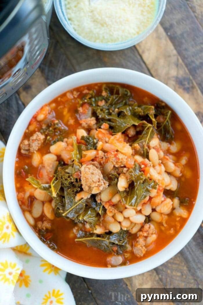Pressure cooker sausage soup is packed with flavor and can be made with or without kale. Using canned or dry beans it's the perfect dinner. #instantpotrecipes #sausagesoup #soup #kale #pressurecooker #instantpot #thetypicalmom #drybeans #sausage A bowl of hearty Italian sausage soup with beans and kale, prepared effortlessly in a pressure cooker, sits on a wooden table next to freshly grated cheese.