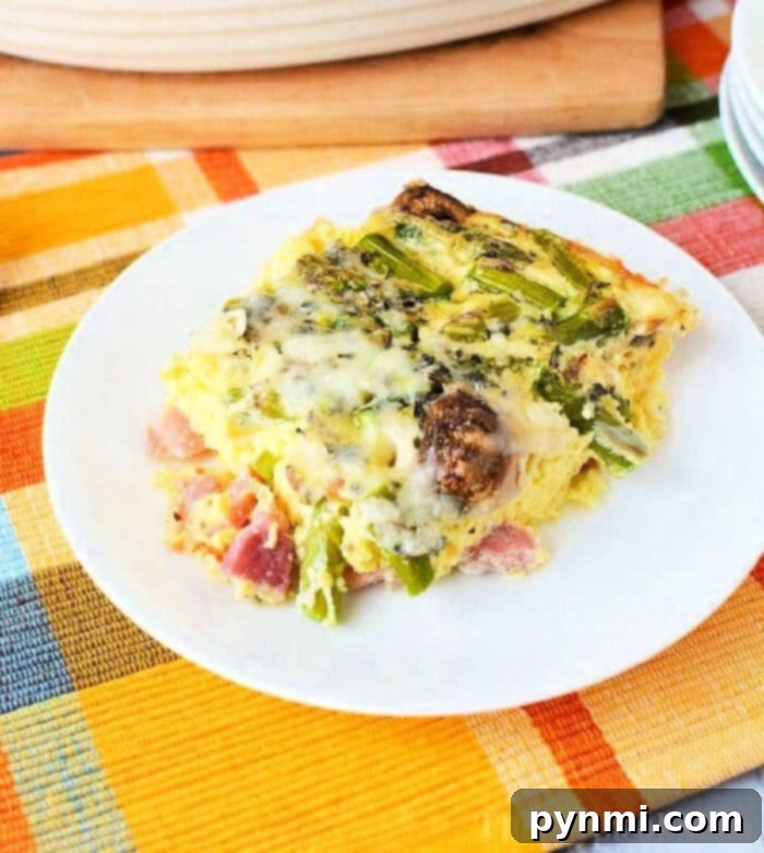 Spring Green Bake 2 A slice of vegetable asparagus egg casserole recipe, rests on a white plate atop a colorful plaid tablecloth.