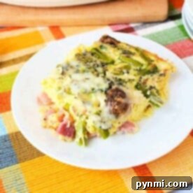 A slice of vegetable asparagus egg casserole recipe, rests on a white plate atop a colorful plaid tablecloth.