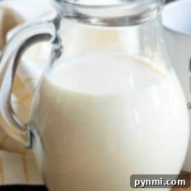 A clear glass pitcher filled with milk and pumpkin spice coffee creamer sits on a wooden table next to a white cloth.