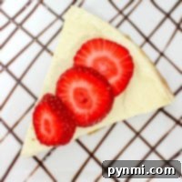 A slice of cheesecake made from an instant pot cheesecake recipe, topped with strawberries and served on a plate drizzled with chocolate sauce in a crisscross pattern.