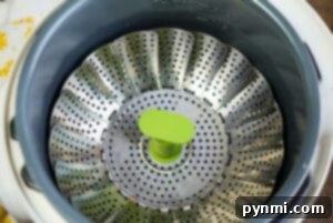 Top view of a metal vegetable steamer basket with a green handle inside an Instant Pot, perfect for boiling potatoes efficiently.