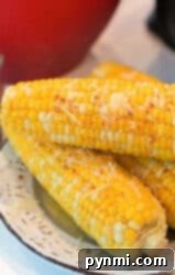 Three ears of corn sprinkled with cheese and seasoning on a white plate showcase a perfect example of how to cook frozen corn on the cob while maintaining vibrant flavors.