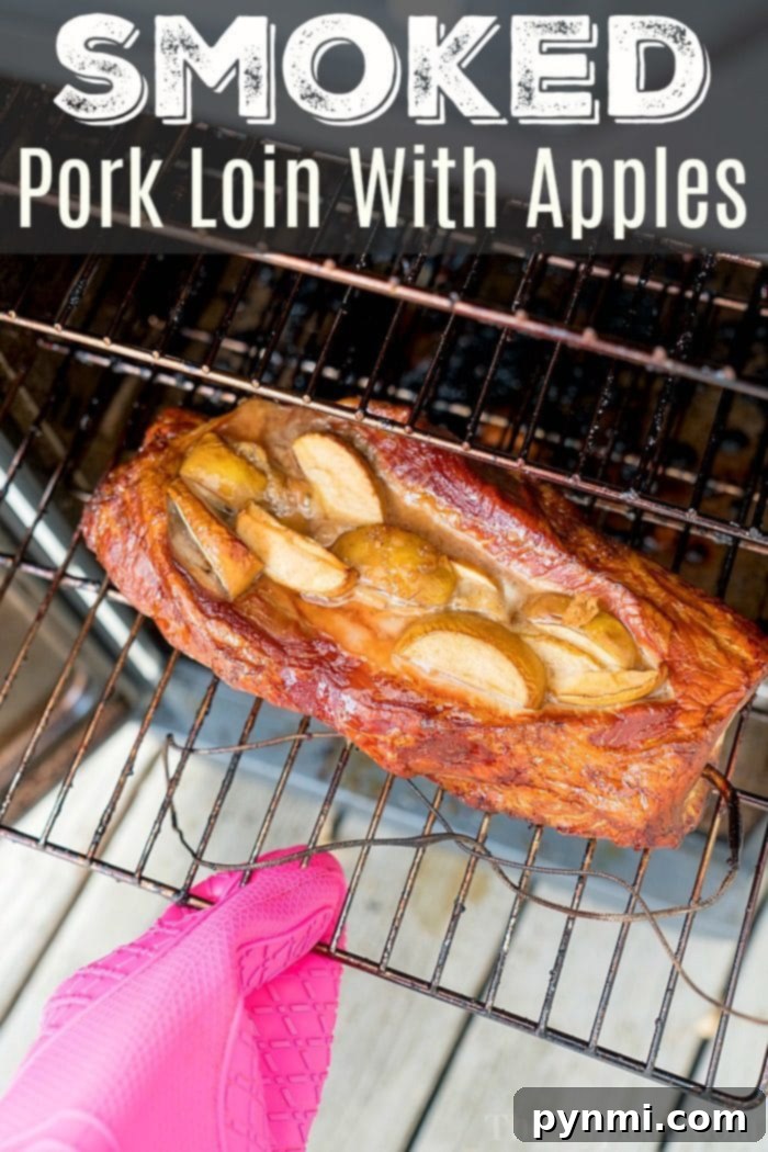 Succulent Smoked Stuffed Pork Loin 2 A perfectly smoked pork loin, artfully topped with golden apple slices, rests on a grill rack. A hand in a pink oven mitt gently holds the rack, showcasing the tender, flavorful results of this incredible smoked pork recipe.