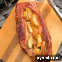 A succulent smoked pork loin, beautifully stuffed with apple slices, rests on a wooden cutting board, ready to be sliced. Tongs are visible nearby, completing this exquisite smoked pork recipe presentation.