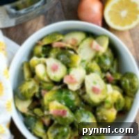 A bowl of Brussels sprouts with crispy bacon sits invitingly next to lemon halves and a shallot, showcasing the simplicity and flavor unlocked by using an Instant Pot.