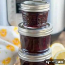 Three small jars of homemade pressure cooker jam are stacked in front of an Instant Pot, with lemon slices beside them.