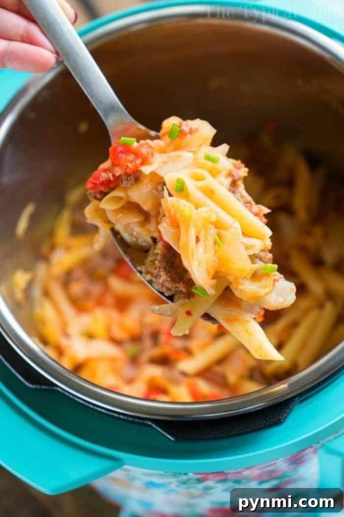 A spoonful of cheesy pasta with ground meat, sausage, and vegetables is being lifted from an Instant Pot. This delightful pressure cooker dish includes penne, chopped tomatoes, cabbage, and garnished green onions. The interior of the pot is also visible.