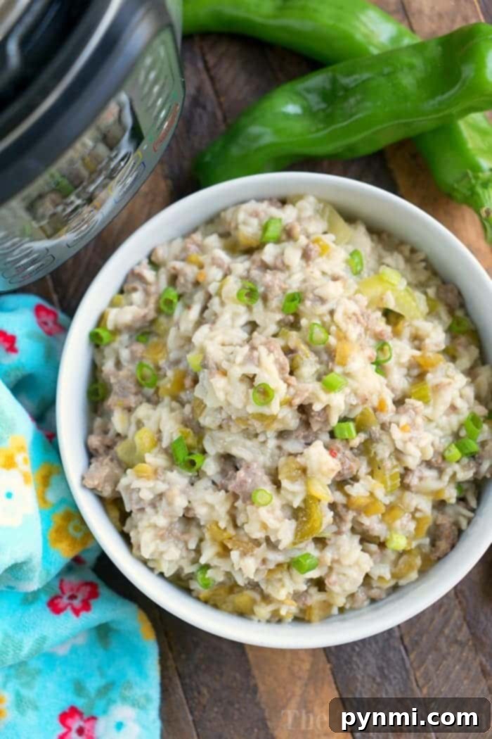 A bowl of creamy rice dish with ground sausage, chopped green peppers, and garnished with fresh green onions. Two whole green peppers and a colorful patterned cloth accompany the bowl on a rustic wooden surface, highlighting a comforting Instant Pot creation.