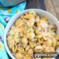 A bowl of creamy pasta shells with ground meat and melted cheese, perfect for meat lovers, garnished with chopped chives. A colorful towel is on the side. An Instant Pot stands proudly in the background on a wooden surface, hinting at this pressure cooker mac and cheese's delicious origin.