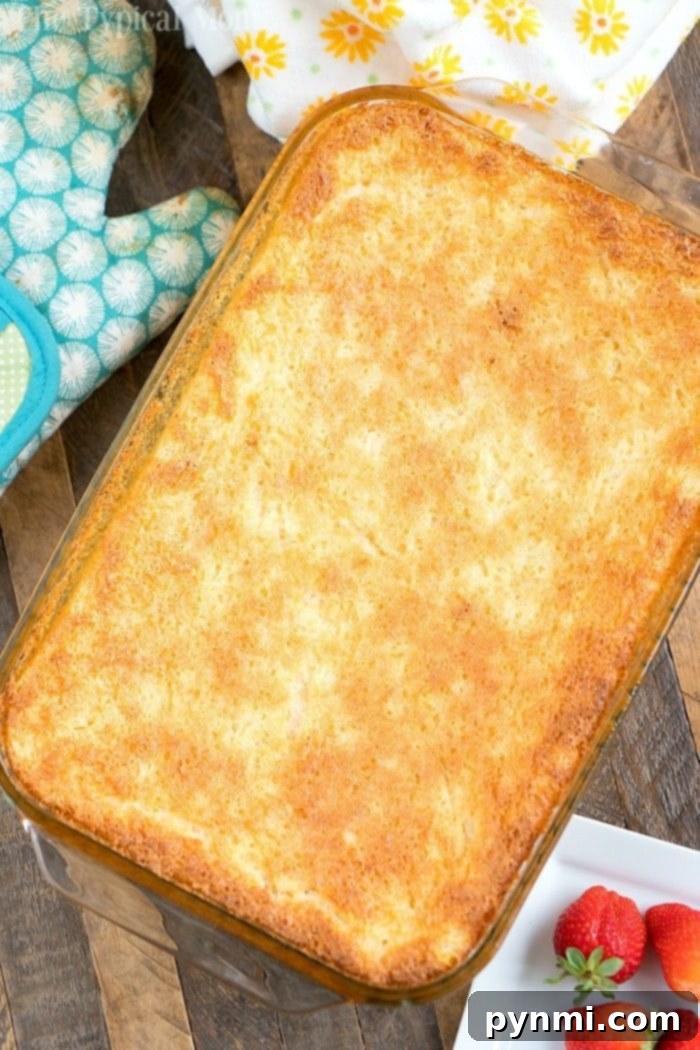 Heavenly Pineapple Delight 4 A golden-brown baked pineapple angel food cake rests in a glass baking dish, with a blue oven mitt and fresh strawberries on a wooden table.