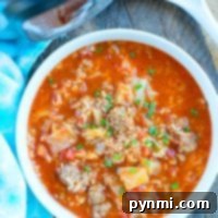 A bowl of hearty pressure cooker cabbage soup with ground meat, tomatoes, and rice sits next to a blue towel.