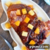 A glazed ham with pineapple chunks sits invitingly on a white platter, reminiscent of a delicious crockpot ham recipe, all elegantly arranged on a wooden table adorned with a blue napkin.
