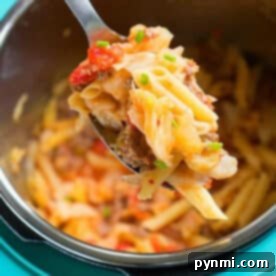 A spoonful of pasta with ground meat and vegetables, reminiscent of a hearty pressure cooker sausage and cabbage dish, held above a pot of pasta.