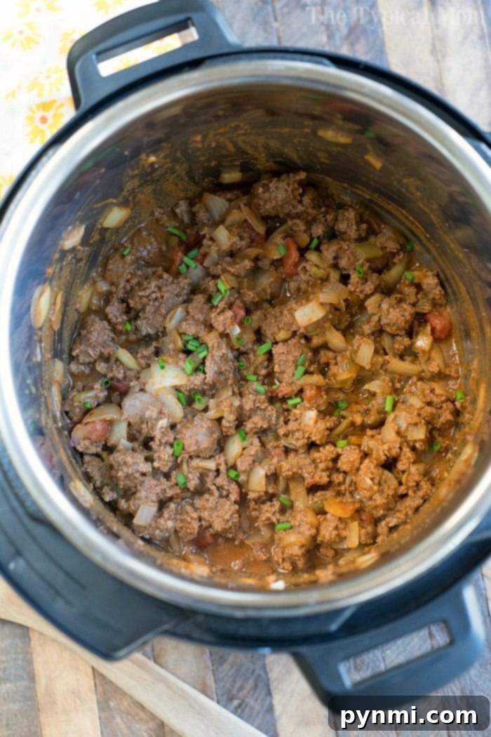 This is how to make the best Instant Pot taco meat with ground beef plus 4 other ways to make Instant Pot tacos you will love. Taco Tuesdays are set! #instantpot #pressurecooker #tacomeat #groundbeef #instantpotrecipes #thetypicalmom Instant Pot taco meat with onions and tomatoes simmering to perfection, garnished with a sprinkle of fresh green onions.