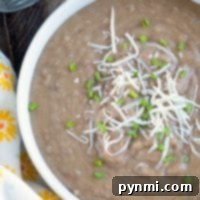 A bowl of creamy pressure cooker refried beans topped with shredded cheese and chopped chives sits next to a floral napkin.