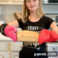 Effortless Whole Wheat Bread in a Bag 3 A girl in a black shirt proudly holds a loaf of whole wheat bread in a bag with red oven mitts, standing confidently in her kitchen.