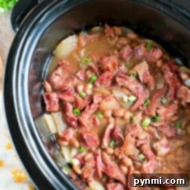 A slow cooker brimming with ham and beans, featuring tender pinto beans, diced ham, and green onions nestled in a savory broth.