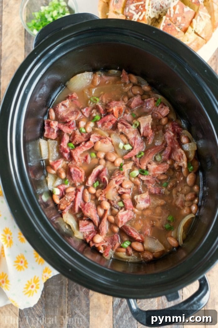 A top-down view of a slow cooker filled with hearty ham and bean soup, garnished with fresh parsley.